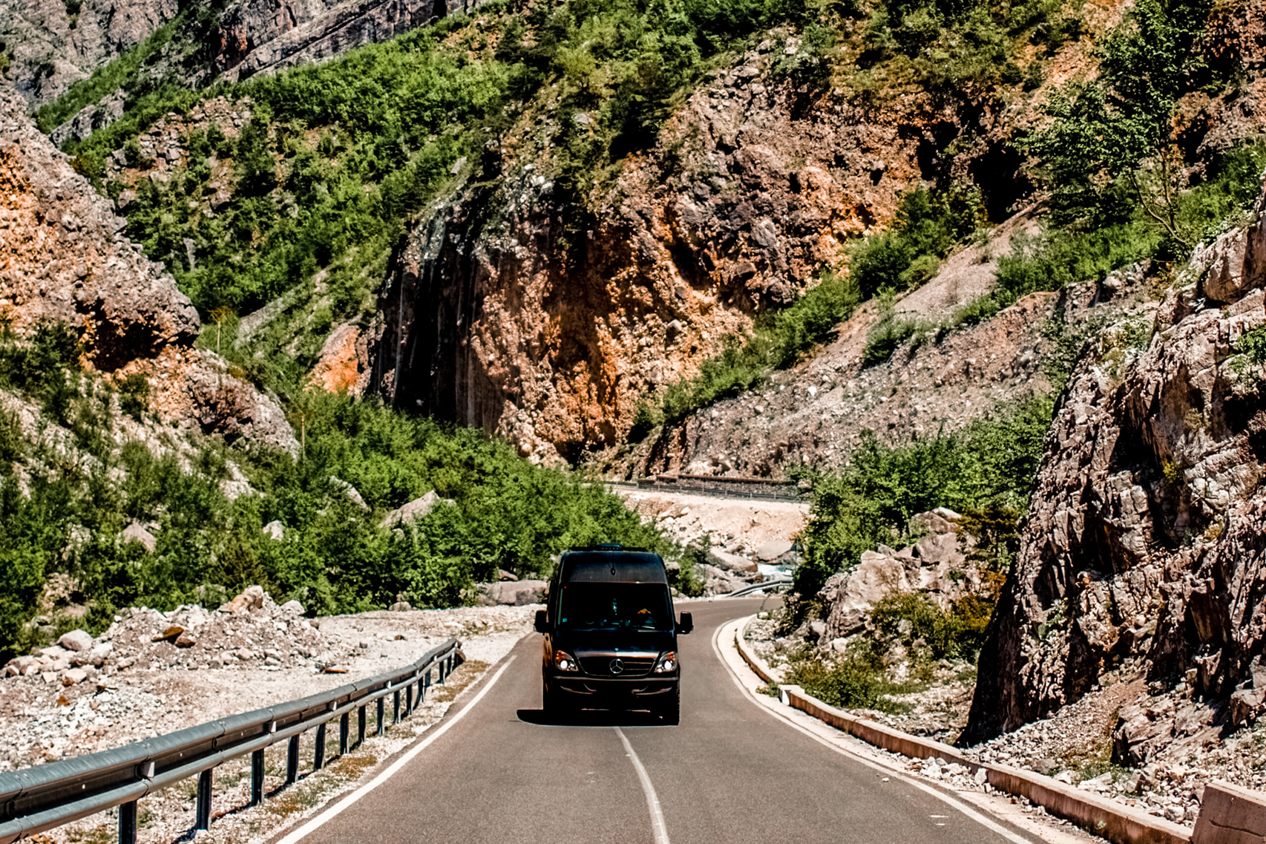 A black sprinter van driving on a highway through mountains