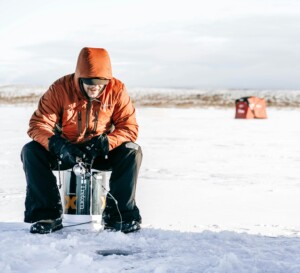 man ice fishing on frozen lake