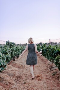 woman walking through vineyard holding wine glass